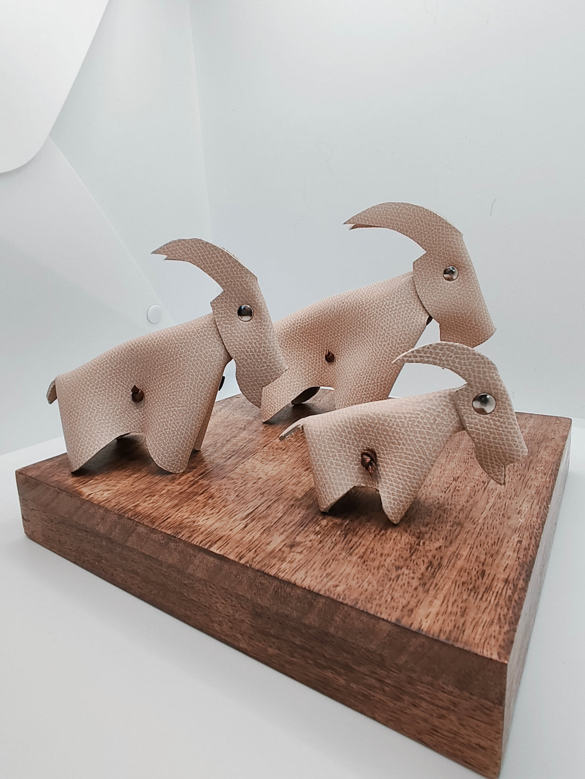Trio de chèvres décoratives en cuir couleur sable, présenté sur un support en bois