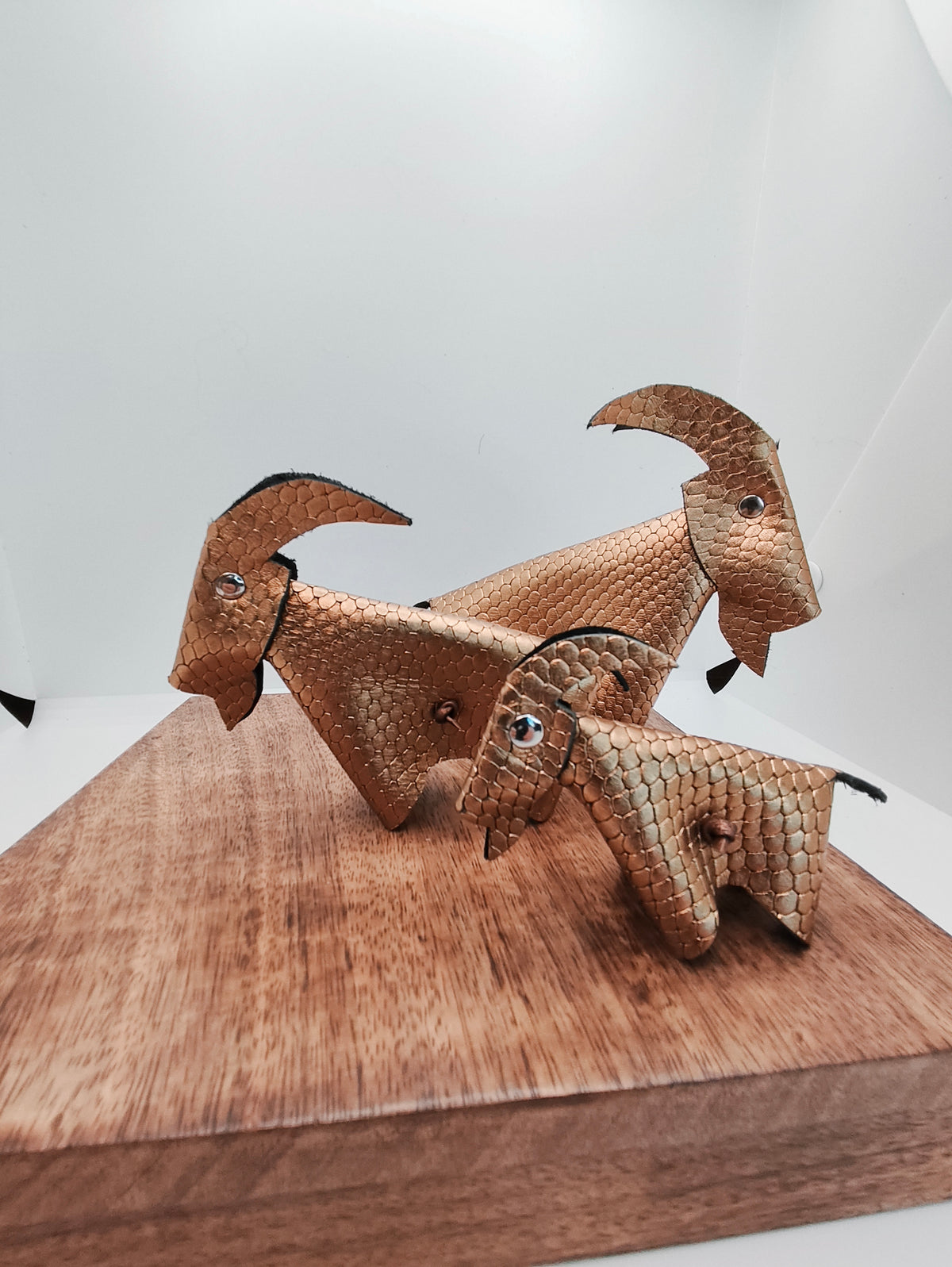 Trio de chèvres décoratives en cuir doré texturé à motif d’écailles, sur un support en bois