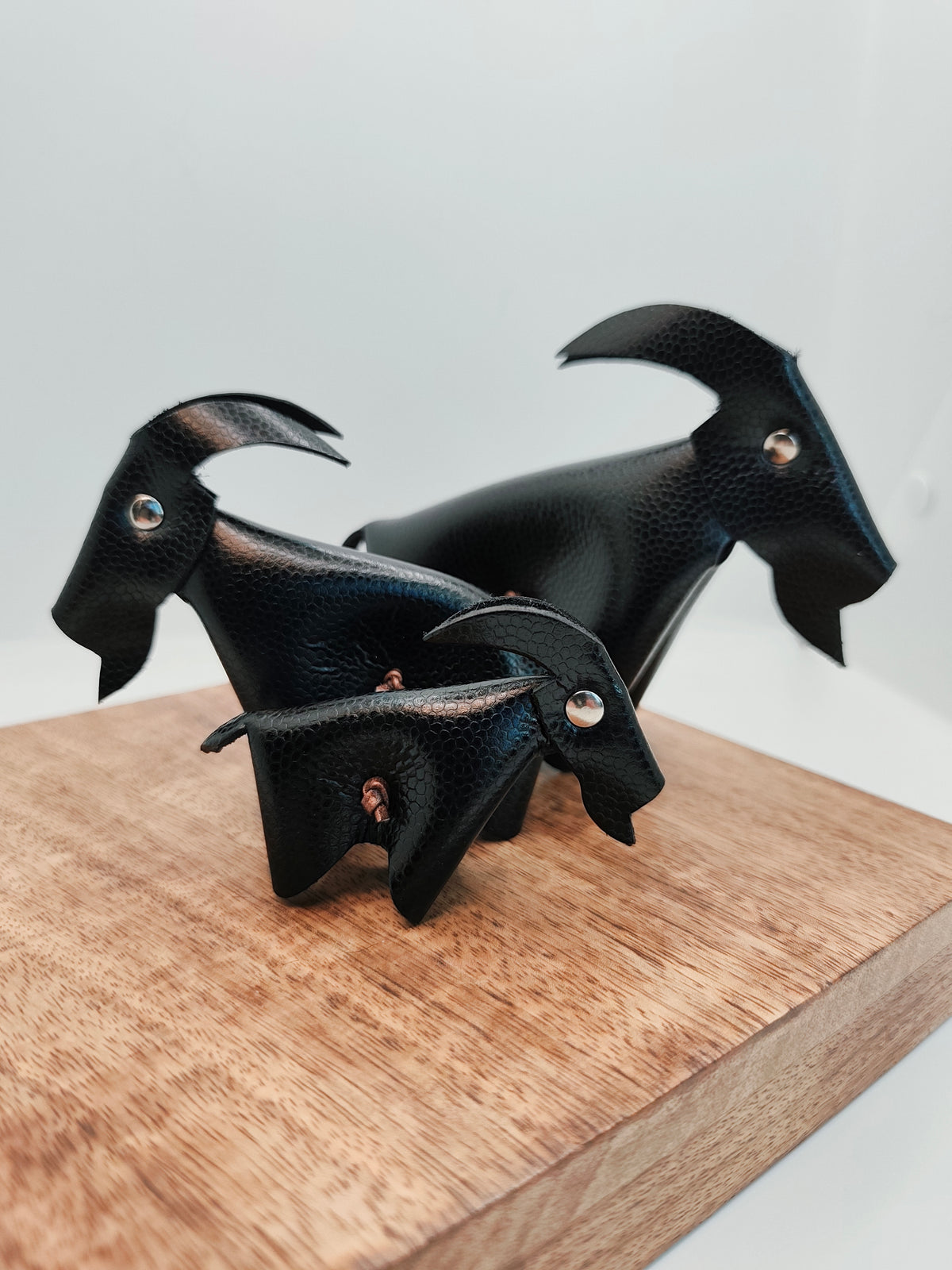 Trio de chèvres en cuir noir grainé, présenté de trois quarts sur un support en bois
