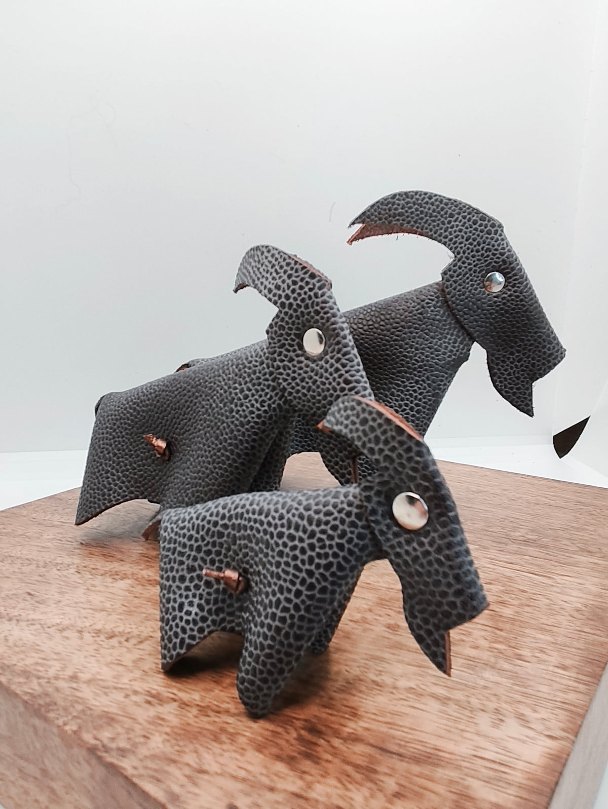 Trio de chèvres décoratives en cuir marron grainé, sur un support en bois