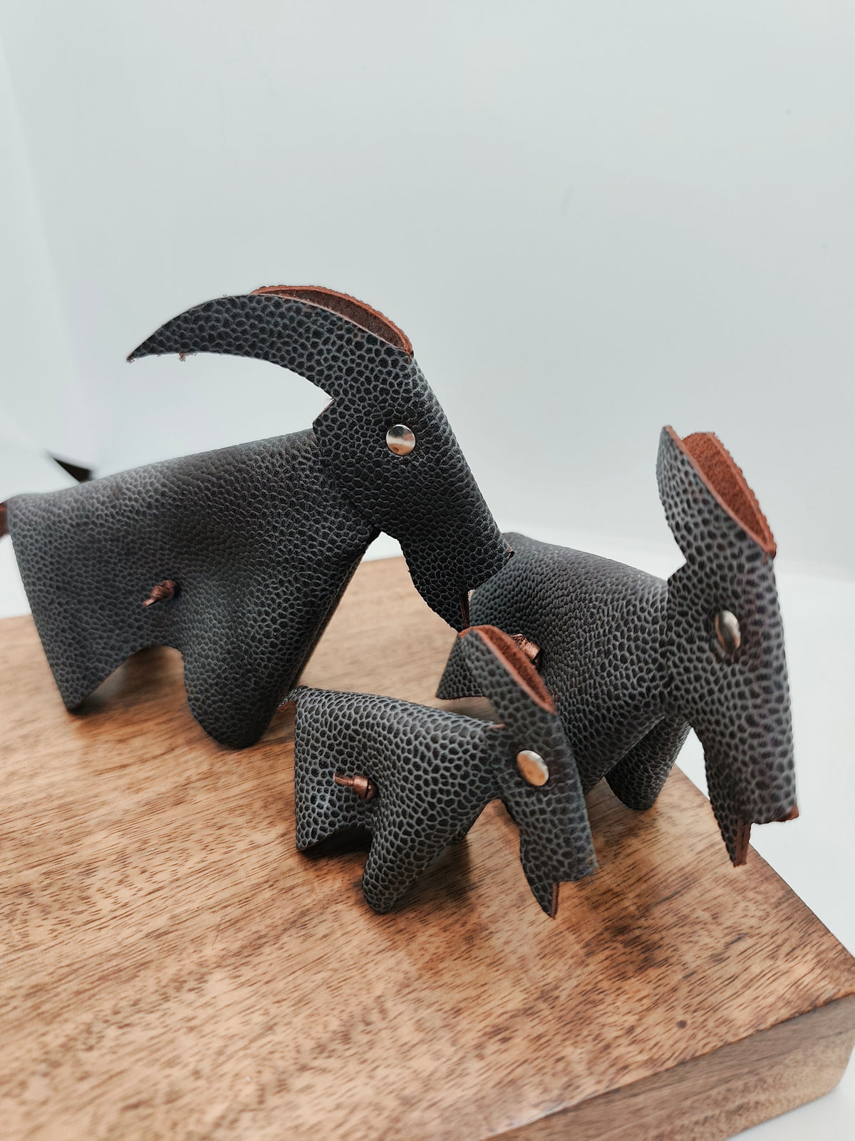 Chèvres en cuir marron grainé de trois tailles, vues sous un autre angle sur un support en bois
