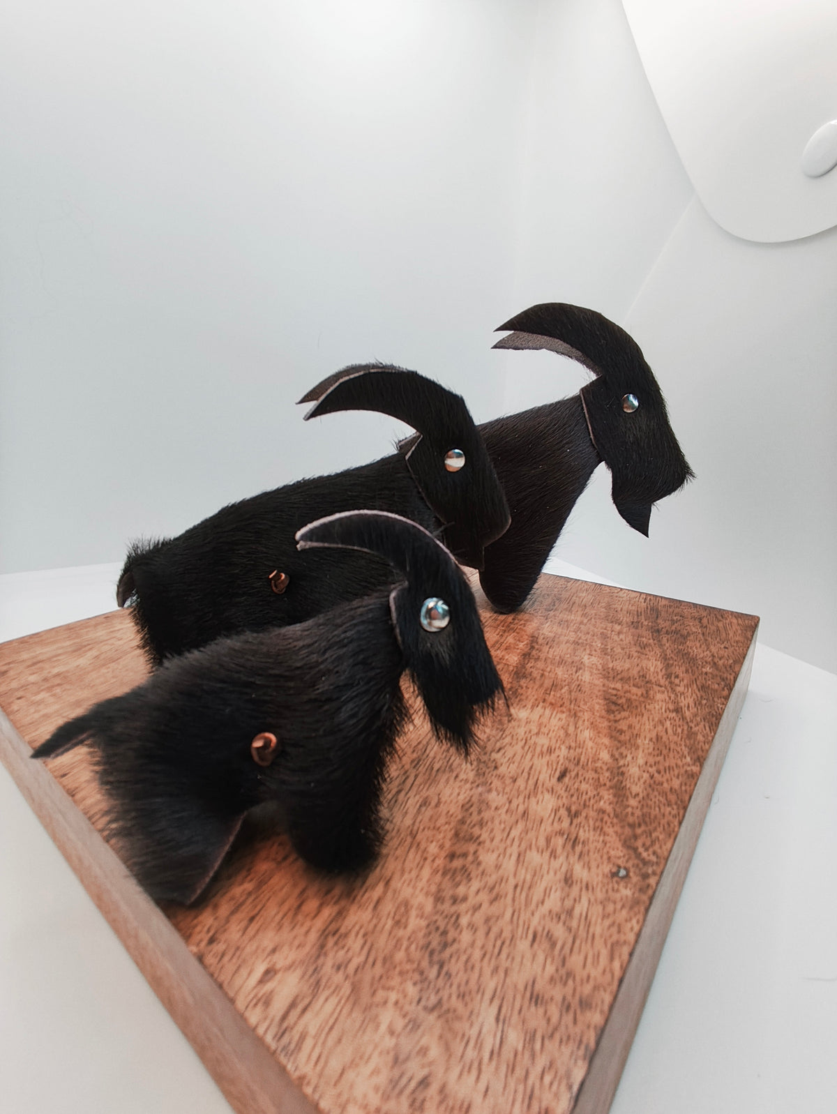 Trio de chèvres décoratives en cuir à pelage noir, sur un support en bois